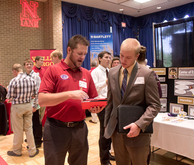 student in suit at career fair booth talking to industry representative.